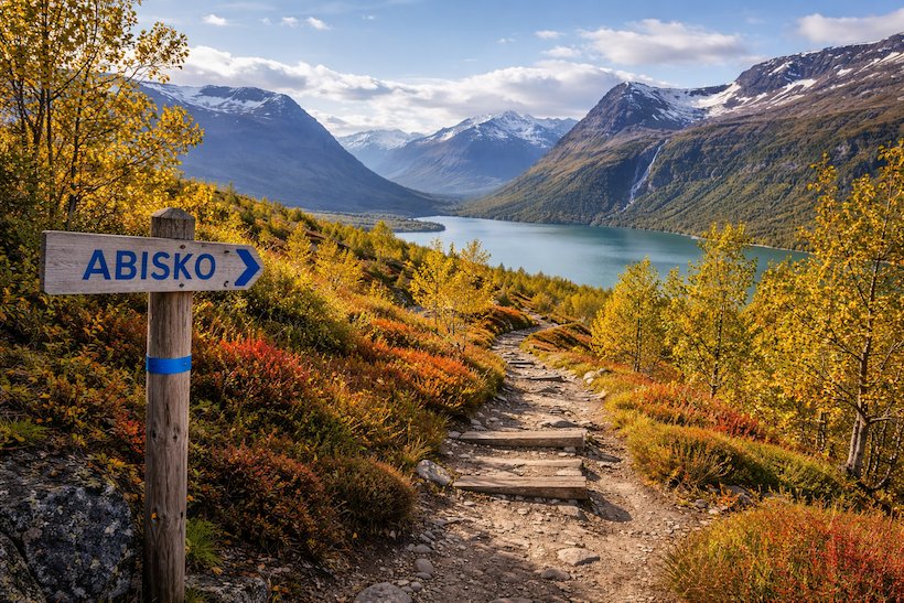 Vandringsled i Abisko med fjällandskap, sjöutsikt och höstfärger längs stigen mot snötäckta berg.
